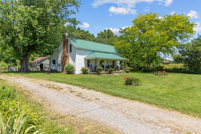 view of front of home featuring a chimney, a porch, a front yard, metal roof, and driveway