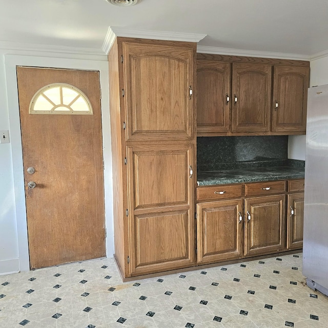 kitchen featuring dark countertops, ornamental molding, brown cabinetry, and freestanding refrigerator