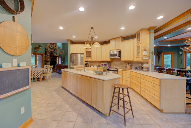 kitchen featuring light brown cabinetry, ornamental molding, a kitchen bar, a center island with sink, and stainless steel appliances