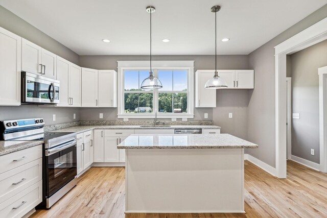 kitchen featuring light hardwood / wood-style flooring, appliances with stainless steel finishes, decorative light fixtures, a kitchen island, and white cabinetry