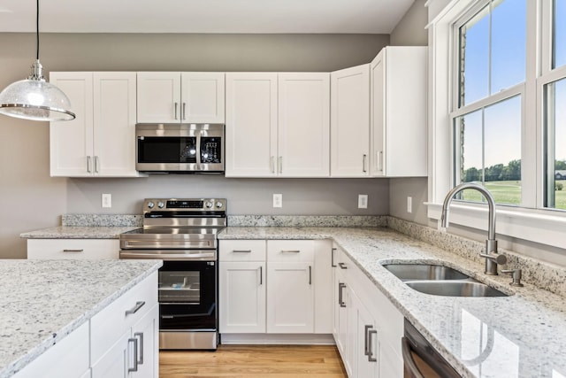 kitchen featuring appliances with stainless steel finishes, white cabinets, a sink, and hanging light fixtures