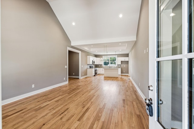 unfurnished living room with light wood-type flooring, baseboards, a raised ceiling, and recessed lighting