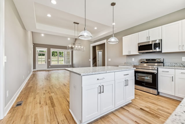 kitchen with decorative light fixtures, stainless steel appliances, white cabinetry, and light hardwood / wood-style floors