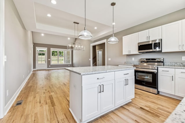 kitchen featuring stainless steel appliances, light wood-type flooring, a raised ceiling, and a kitchen island