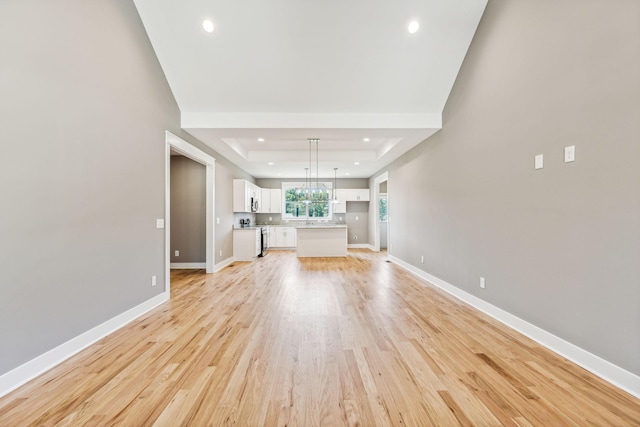 unfurnished living room with a tray ceiling, recessed lighting, light wood-style flooring, and baseboards