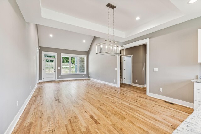 unfurnished dining area with a chandelier, a tray ceiling, and light hardwood / wood-style flooring