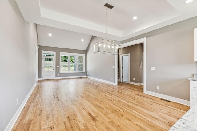 interior space featuring recessed lighting, a raised ceiling, baseboards, and light wood finished floors