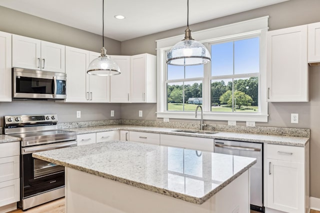 kitchen with a sink, a center island, white cabinets, appliances with stainless steel finishes, and light stone countertops