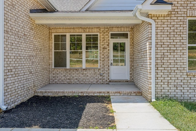 doorway to property featuring a shingled roof and brick siding