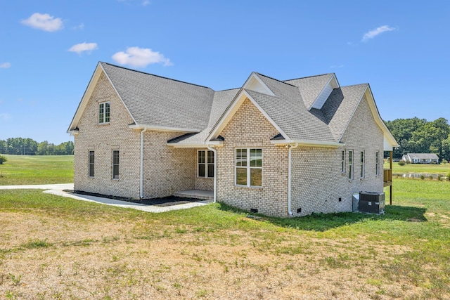 rear view of house with central AC unit, roof with shingles, crawl space, a yard, and brick siding