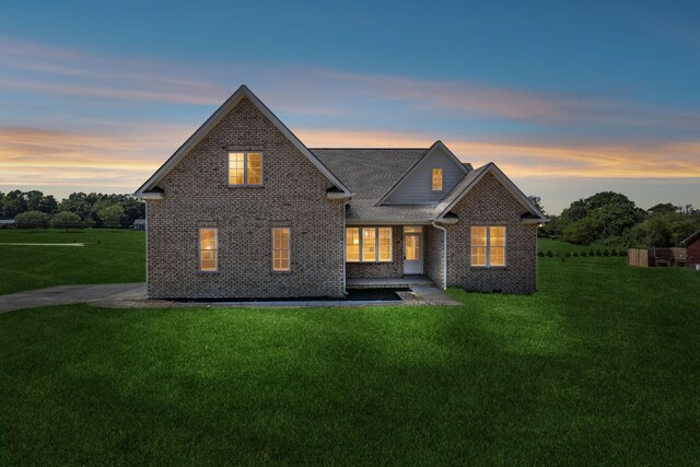 back house at dusk featuring a lawn