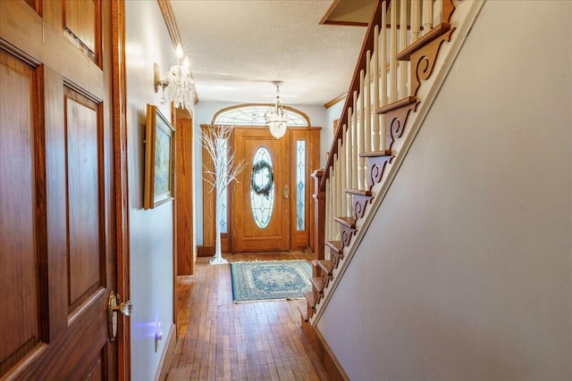 entryway with a textured ceiling, a notable chandelier, hardwood / wood-style floors, and ornamental molding