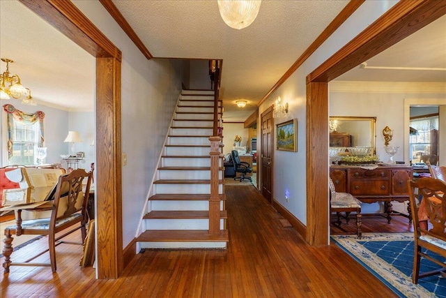 staircase with a textured ceiling, a healthy amount of sunlight, ornamental molding, and wood-type flooring