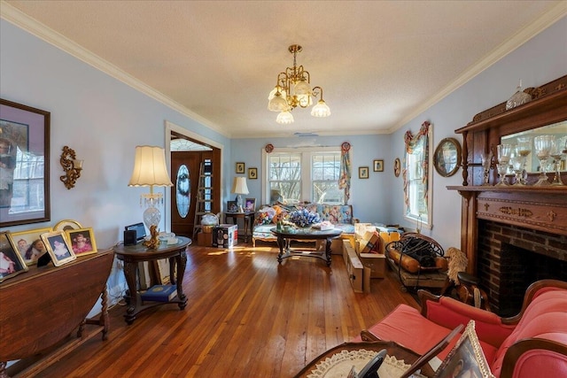 living room with a notable chandelier, crown molding, wood-type flooring, and a brick fireplace