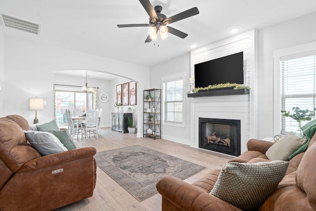 living room with ceiling fan with notable chandelier, light wood-type flooring, and a fireplace