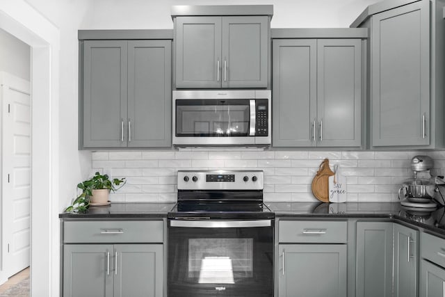 kitchen with gray cabinets, dark stone countertops, tasteful backsplash, and stainless steel appliances