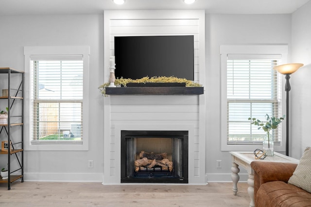 living room with a healthy amount of sunlight, light hardwood / wood-style flooring, and a large fireplace