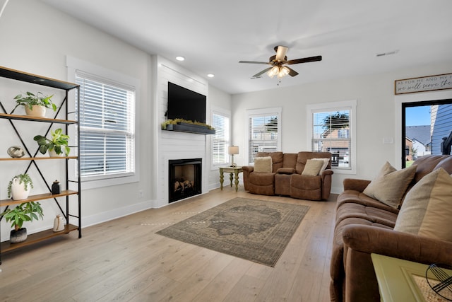 living room with light wood-type flooring, ceiling fan, and a large fireplace