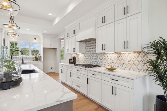 kitchen with light stone countertops, decorative light fixtures, ventilation hood, decorative backsplash, and light wood-type flooring