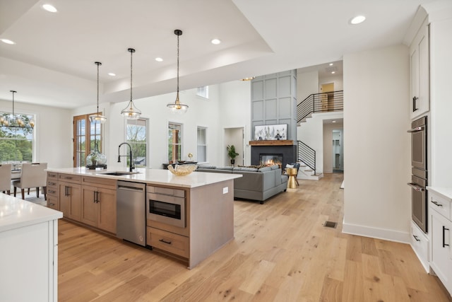 kitchen featuring a kitchen island with sink, stainless steel appliances, white cabinetry, and light hardwood / wood-style floors