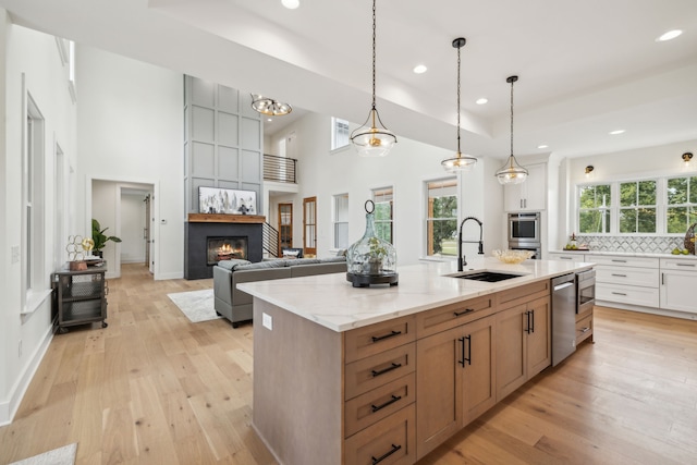 kitchen featuring a kitchen island with sink, a high ceiling, decorative light fixtures, sink, and light hardwood / wood-style floors