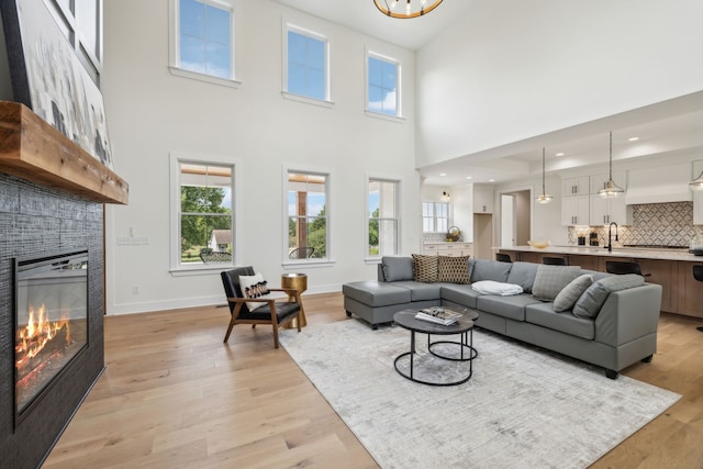 living room featuring a fireplace, sink, a high ceiling, and light hardwood / wood-style floors