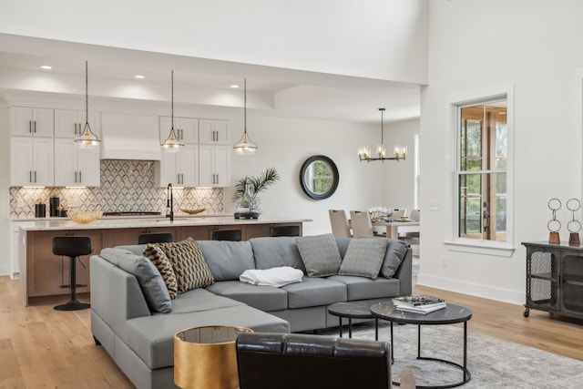 living room with light hardwood / wood-style flooring, sink, a high ceiling, and a notable chandelier