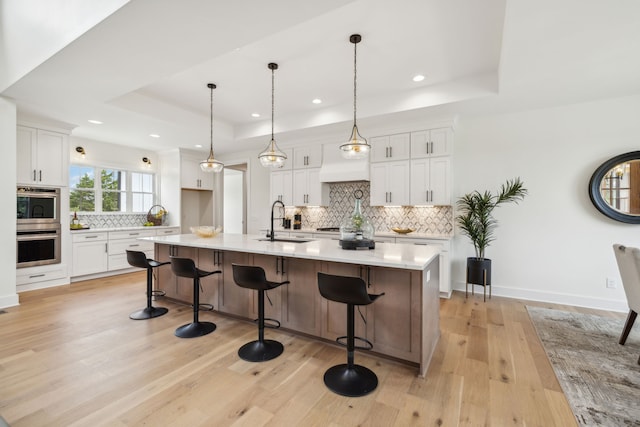 kitchen with decorative backsplash, light hardwood / wood-style floors, white cabinetry, and a center island with sink