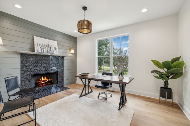 home office featuring a fireplace, light hardwood / wood-style flooring, and wood walls