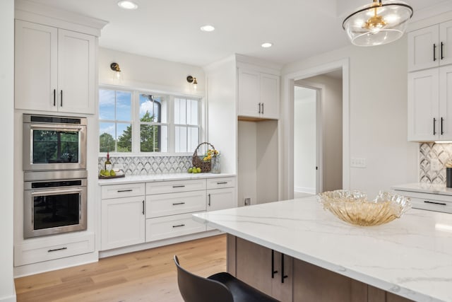 kitchen with white cabinets, backsplash, light hardwood / wood-style flooring, light stone countertops, and double wall oven