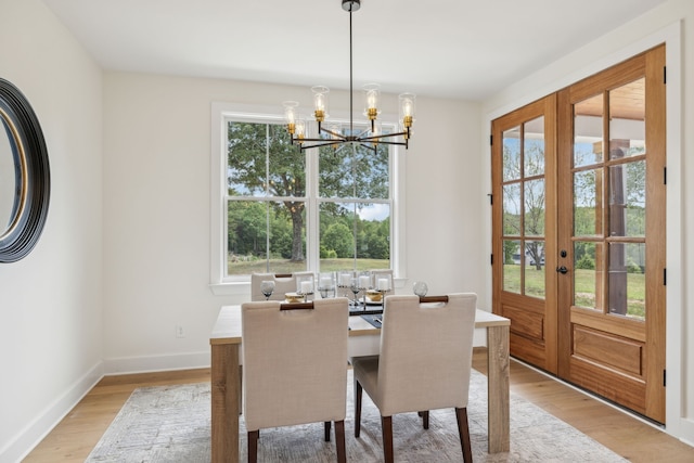 dining area with light wood-type flooring, french doors, a notable chandelier, and a healthy amount of sunlight