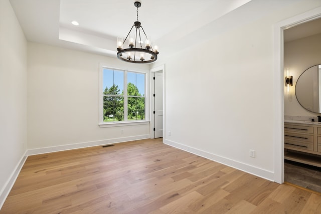 spare room with light hardwood / wood-style flooring, an inviting chandelier, and a tray ceiling