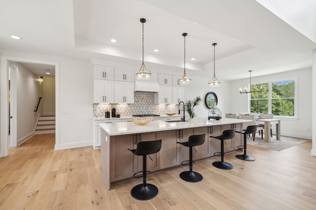 kitchen featuring white cabinets, decorative light fixtures, a large island with sink, light hardwood / wood-style floors, and a raised ceiling