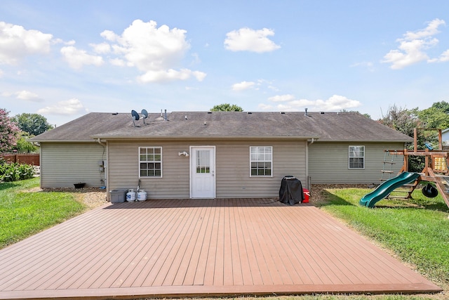 rear view of property featuring a playground, a yard, and a deck