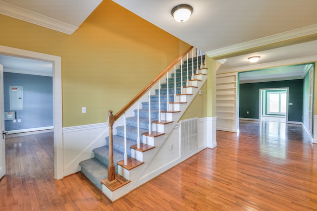 staircase with crown molding, wood-type flooring, built in shelves, and electric panel