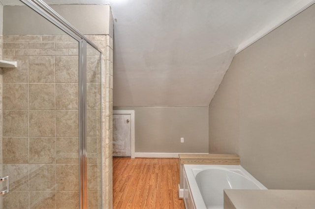 bathroom featuring hardwood / wood-style floors, lofted ceiling, and a tub to relax in