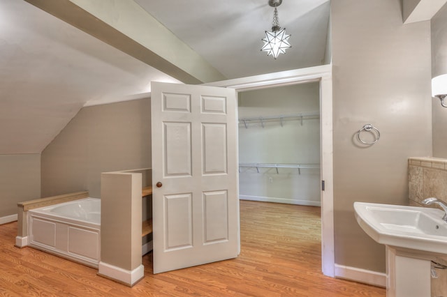 bathroom featuring wood-type flooring, vaulted ceiling, and a tub to relax in