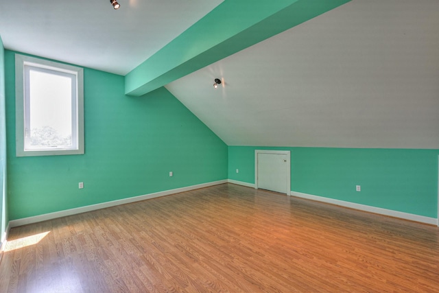 additional living space with light hardwood / wood-style flooring and vaulted ceiling with beams