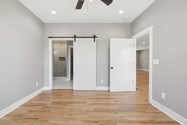 unfurnished bedroom with ensuite bathroom, a barn door, ceiling fan, and light hardwood / wood-style flooring