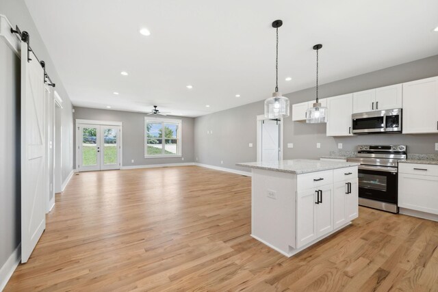 kitchen with white cabinets, hanging light fixtures, a barn door, appliances with stainless steel finishes, and light hardwood / wood-style floors