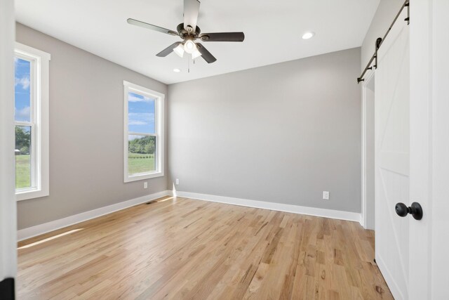 spare room featuring a barn door, ceiling fan, and light hardwood / wood-style flooring