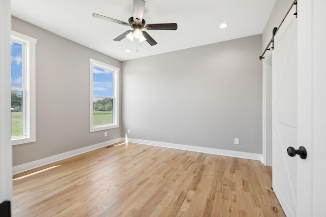 unfurnished bedroom featuring a barn door, recessed lighting, a ceiling fan, baseboards, and light wood finished floors