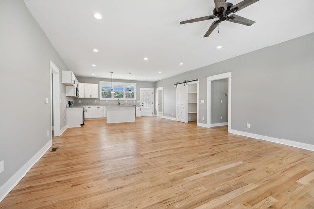 unfurnished living room with a barn door, light hardwood / wood-style flooring, ceiling fan, and sink