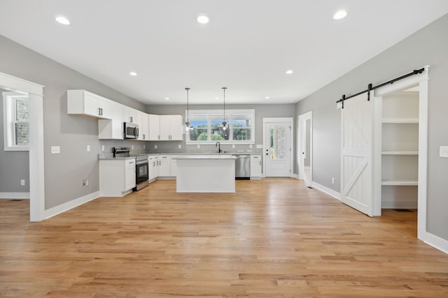 kitchen with a barn door, white cabinets, light wood-type flooring, and appliances with stainless steel finishes