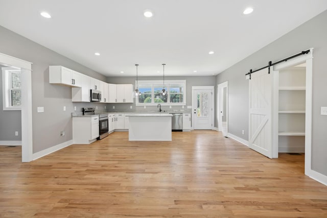 kitchen with stainless steel appliances, light countertops, a barn door, white cabinets, and a sink