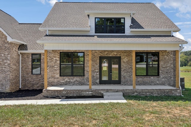 view of exterior entry with french doors, brick siding, a yard, roof with shingles, and covered porch