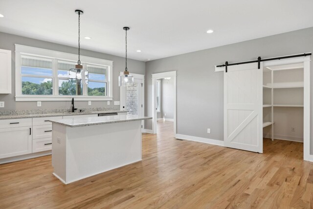 kitchen featuring light wood-type flooring, a kitchen island, a barn door, white cabinetry, and hanging light fixtures