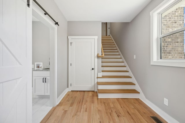 staircase with a barn door, visible vents, baseboards, and wood finished floors