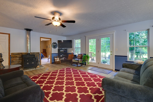 living room featuring a wood stove, ceiling fan, hardwood / wood-style flooring, and a textured ceiling