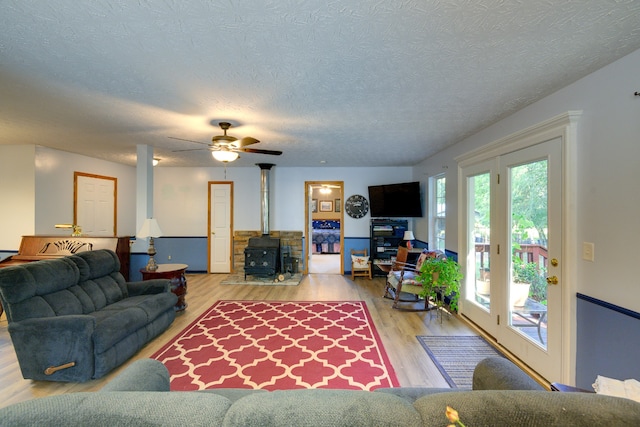 living room with a wood stove, ceiling fan, hardwood / wood-style flooring, and a textured ceiling